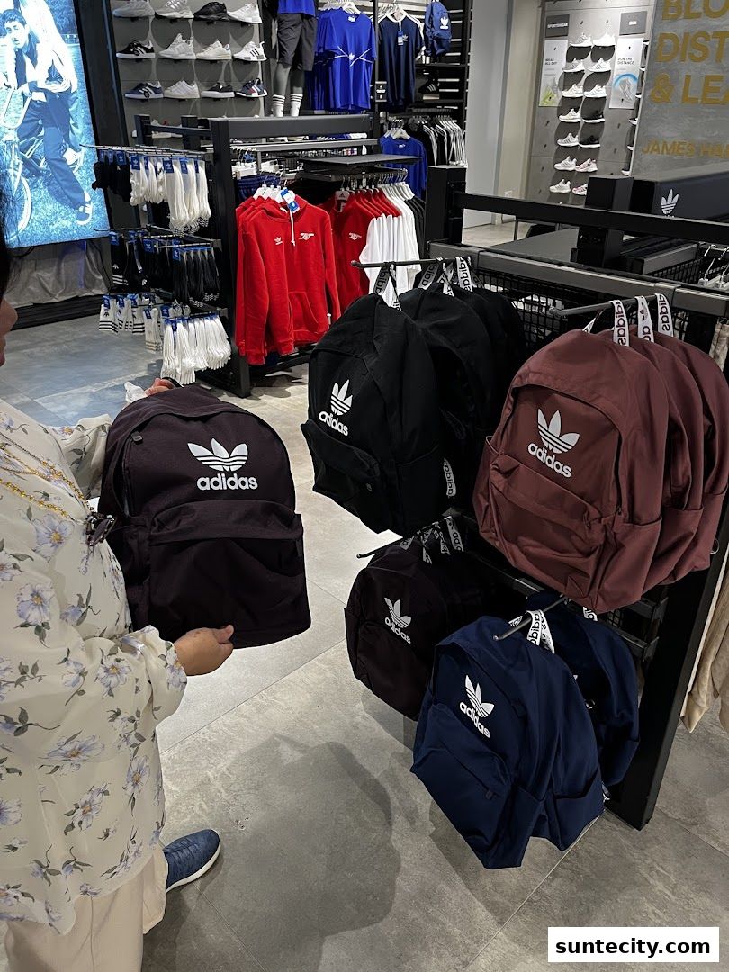 A person browsing Adidas backpacks and apparel inside a store.