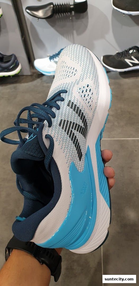 A close-up shot of a white and blue running shoe held by a person wearing a black watch.