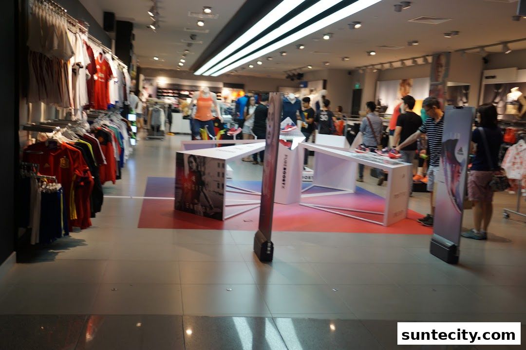 Interior view of an Adidas store with sportswear and shoes displayed, and customers browsing.