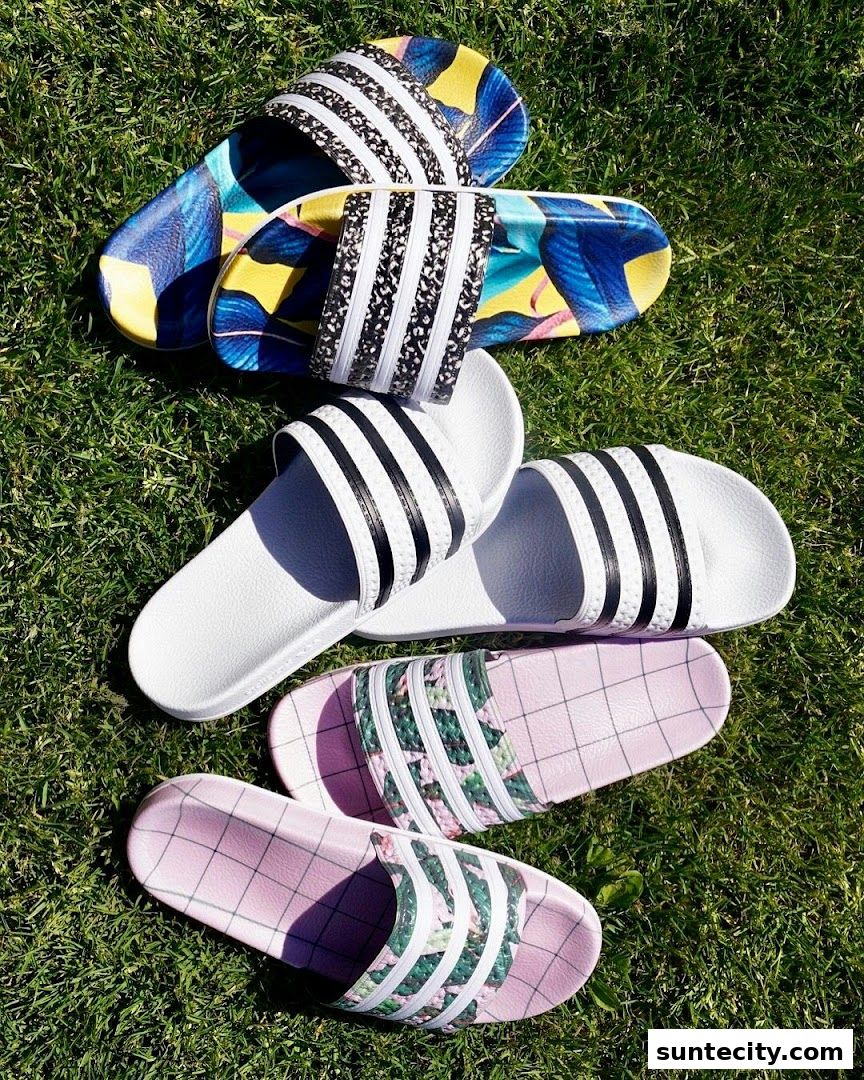 A collection of Adidas slides with various colorful and patterned designs displayed on green grass.