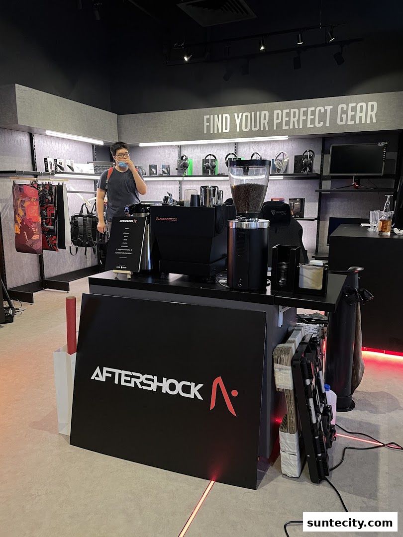 A person stands near a coffee machine and shelves stocked with gaming accessories in a modern retail store.