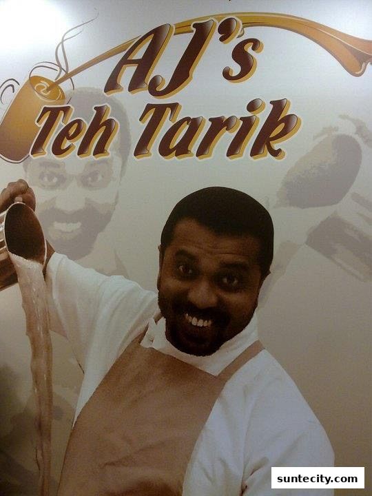 A man in an apron pours a frothy beverage, with the shop name "AJ's Teh Tarik" visible.