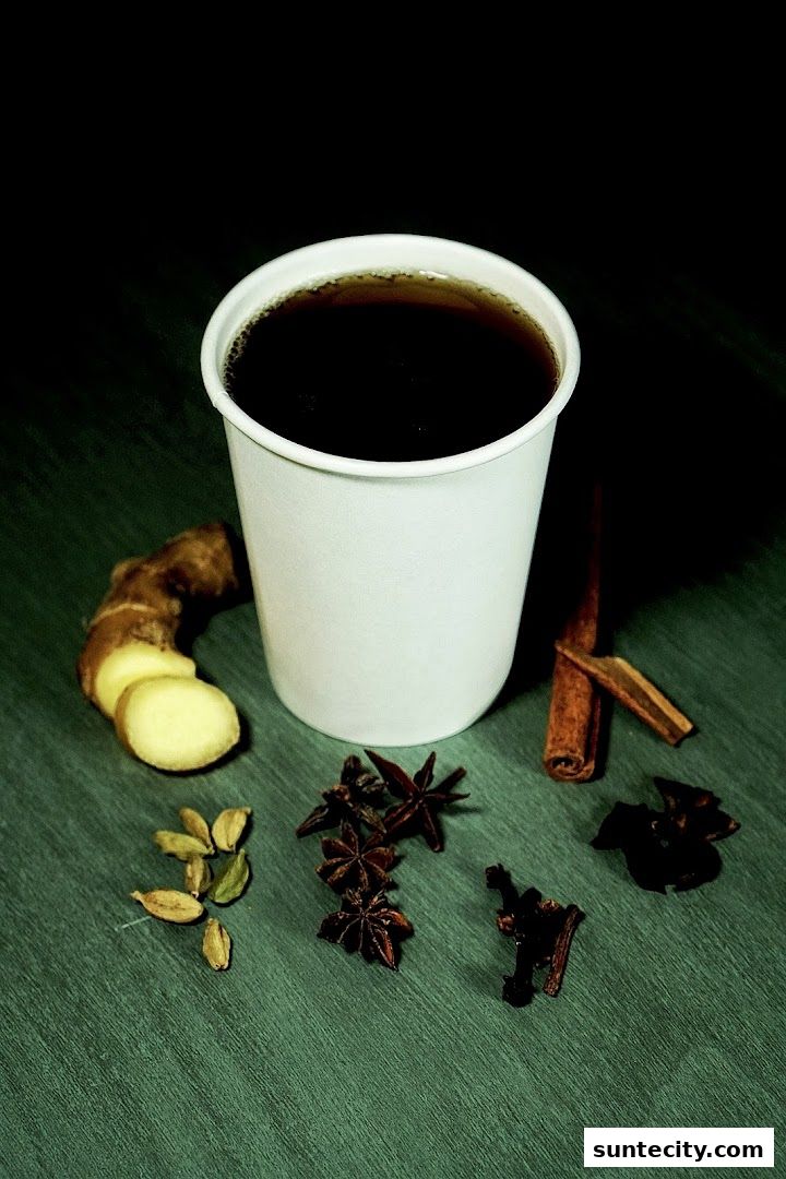 A cup of dark beverage with ginger, cardamom, star anise, and cinnamon sticks.