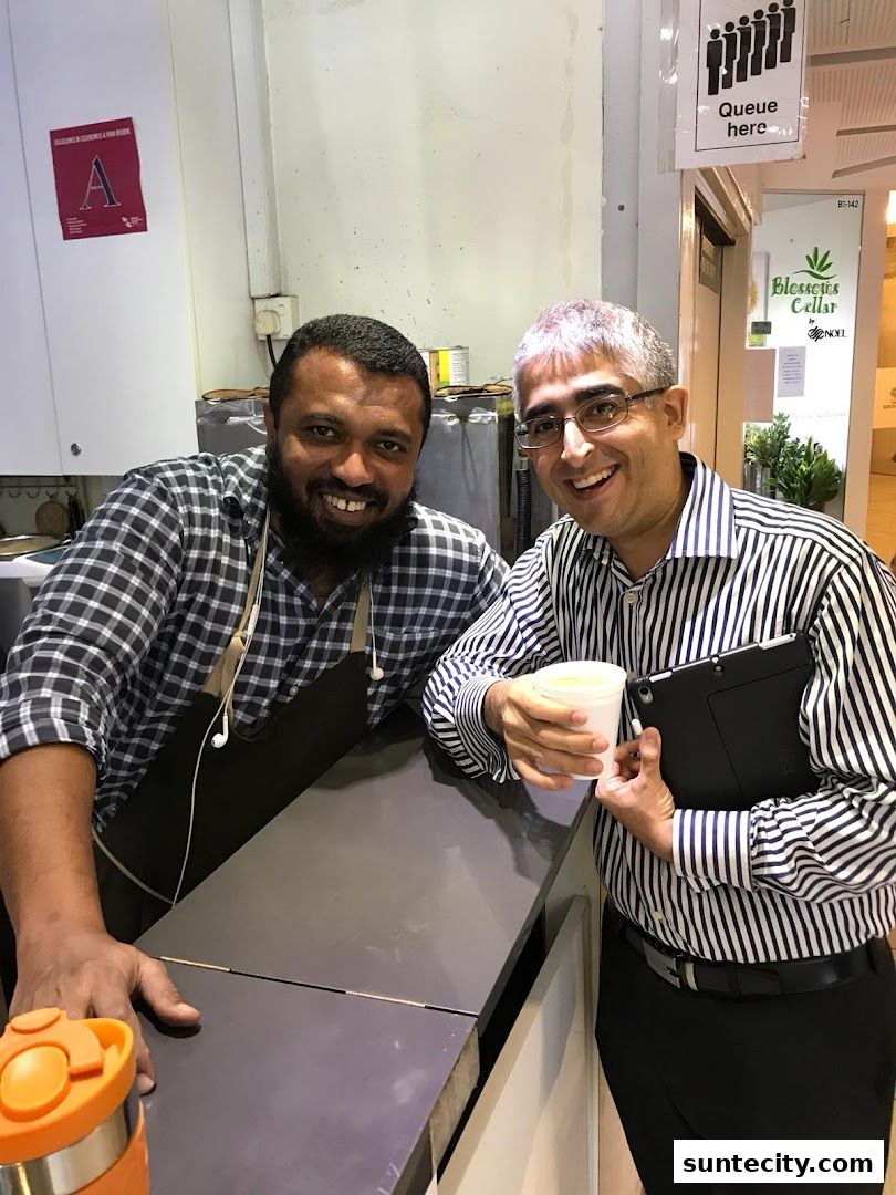 Two smiling men, one behind a counter, pose for a photo at AJs Teh Tarik.