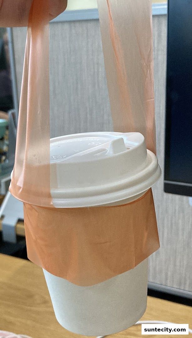 A white paper cup with a white lid, held by an orange plastic bag.