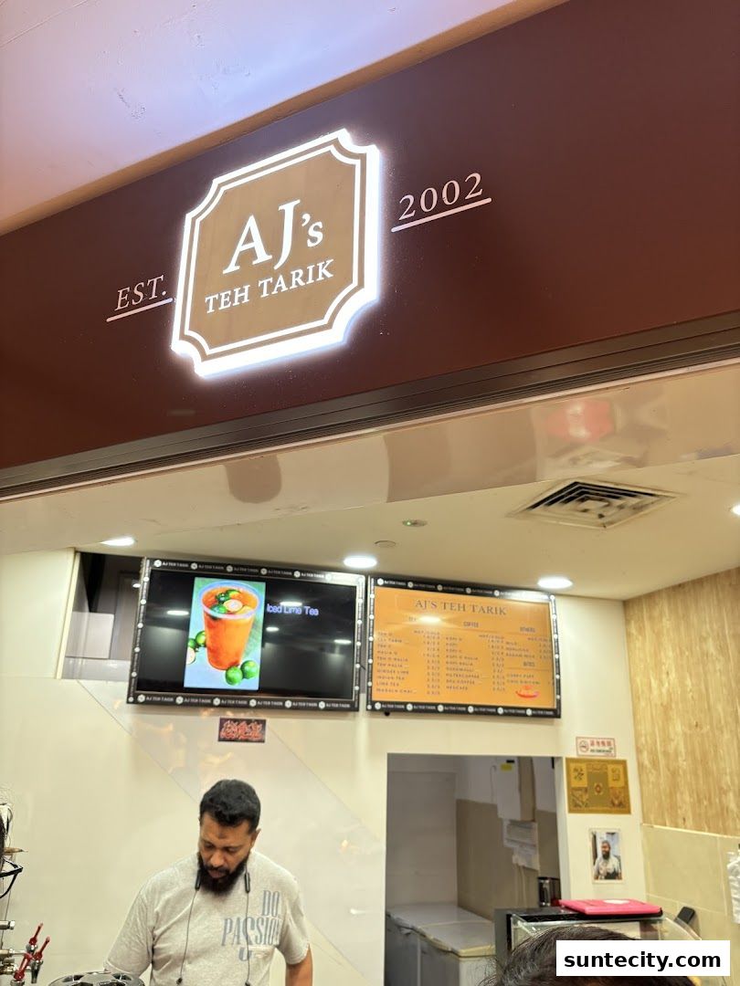 The entrance of AJ's Teh Tarik, featuring a prominent sign and digital menus displaying drinks and prices.