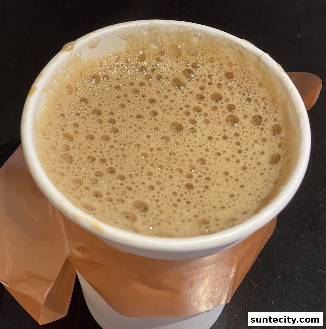 A close-up shot of a frothy, hot beverage in a white paper cup.