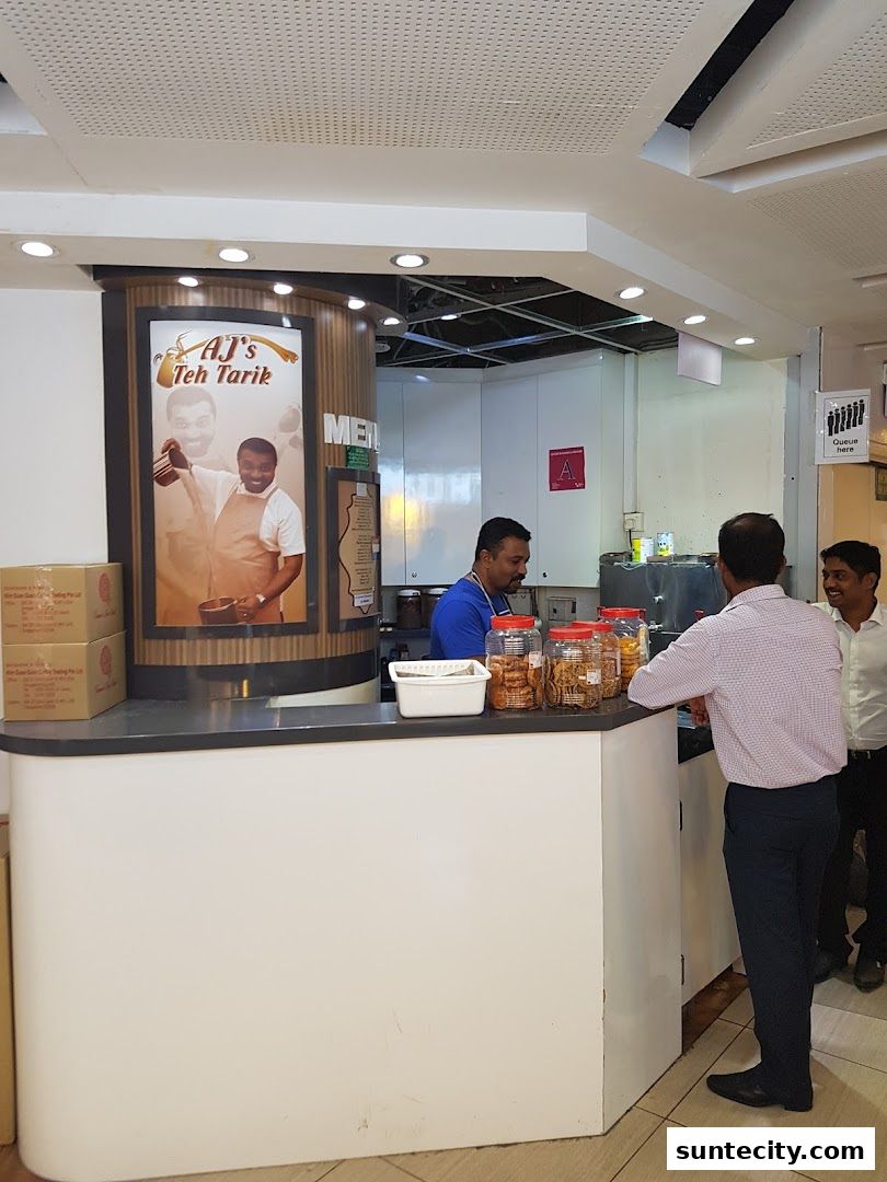 AJs Teh Tarik shop counter with staff and customers, featuring a large promotional poster.