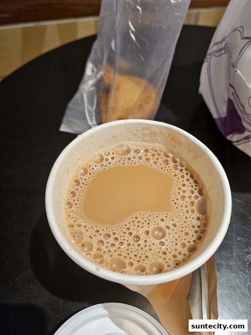 A cup of frothy teh tarik with a pastry in a plastic bag.