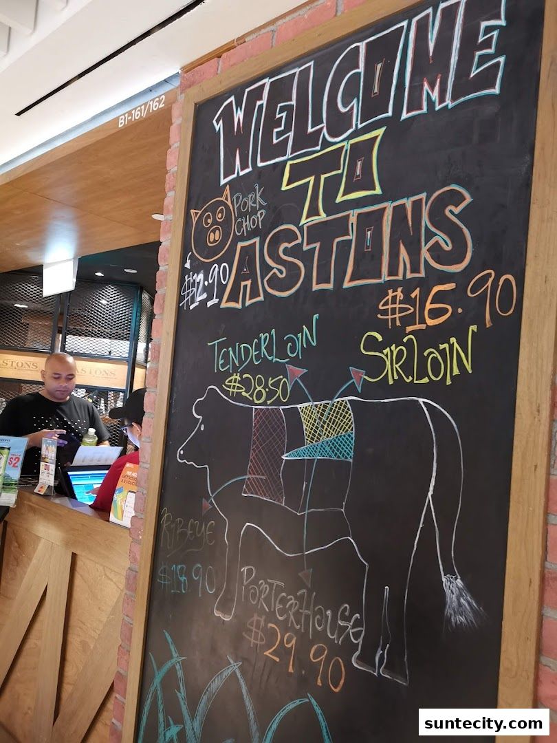 A chalkboard menu displays various steak cuts and prices at ASTONS Specialities.