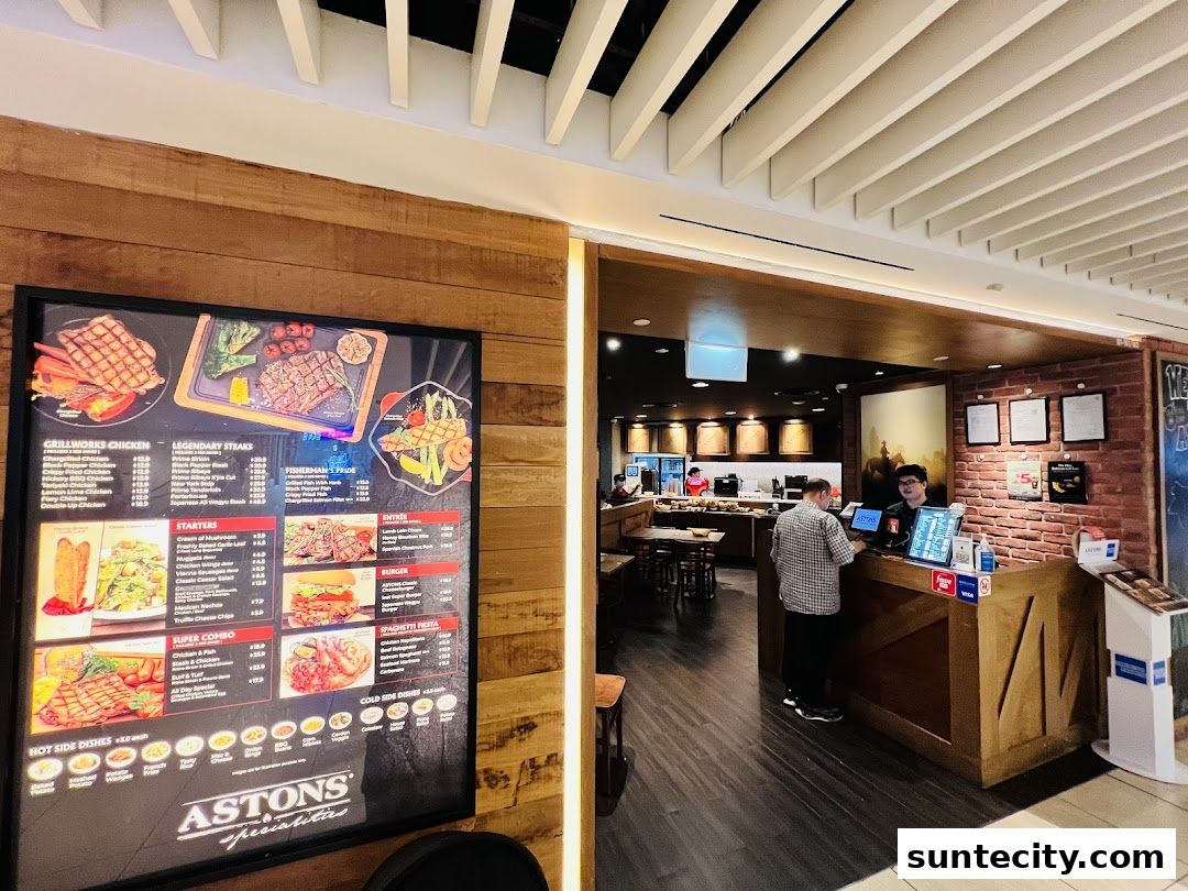 A menu board displays various steak and chicken dishes outside a restaurant with staff at the counter.