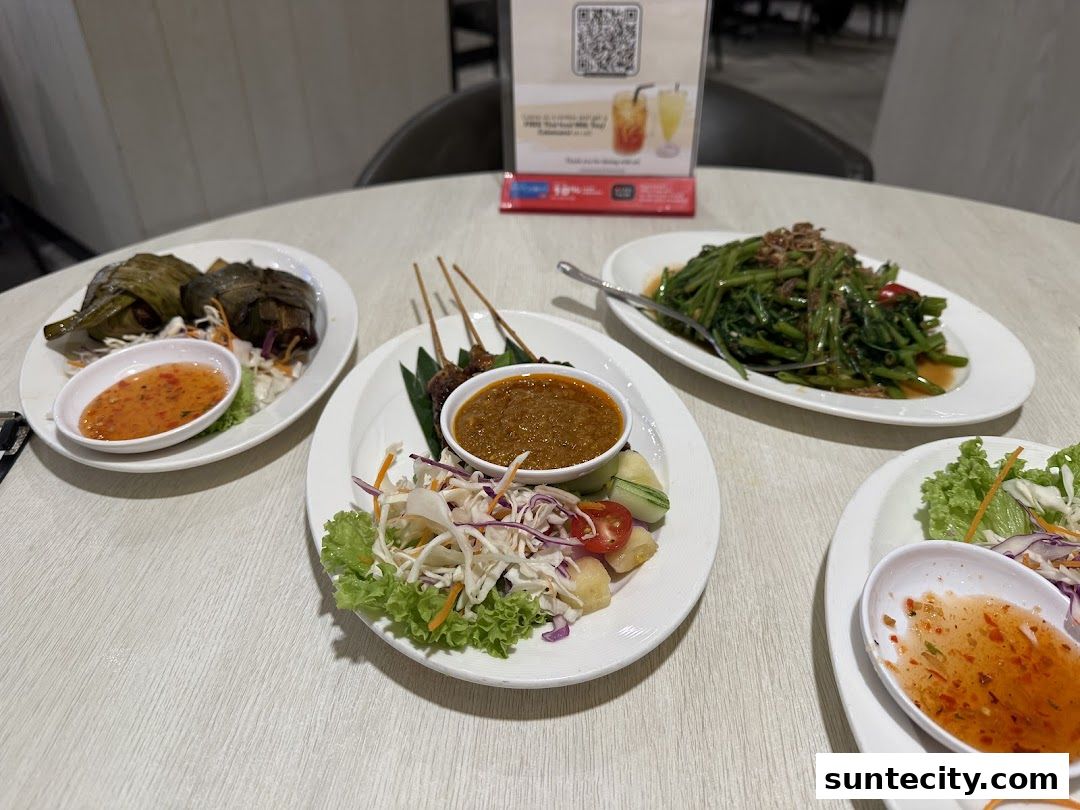 A table laden with delicious Thai dishes, including satay, stir-fried vegetables, and pandan chicken.