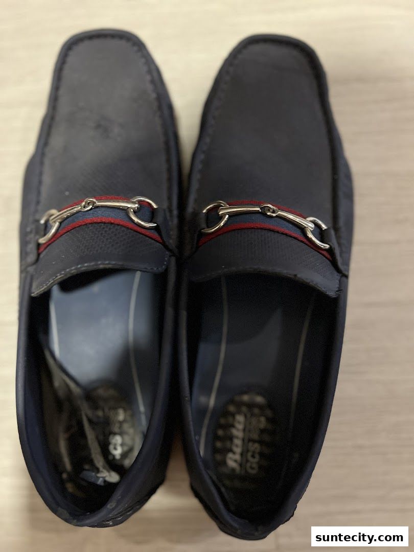 A pair of stylish navy blue loafers with a decorative metal buckle and striped accent.