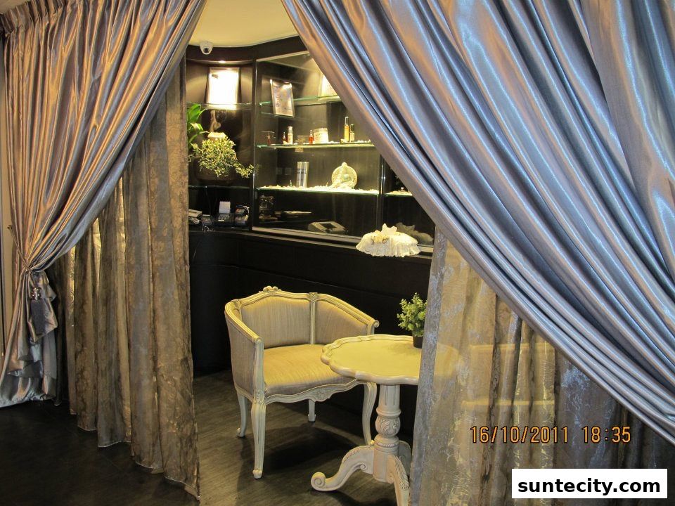 A seating area with a chair and table, framed by elegant curtains, with a display cabinet in the background.