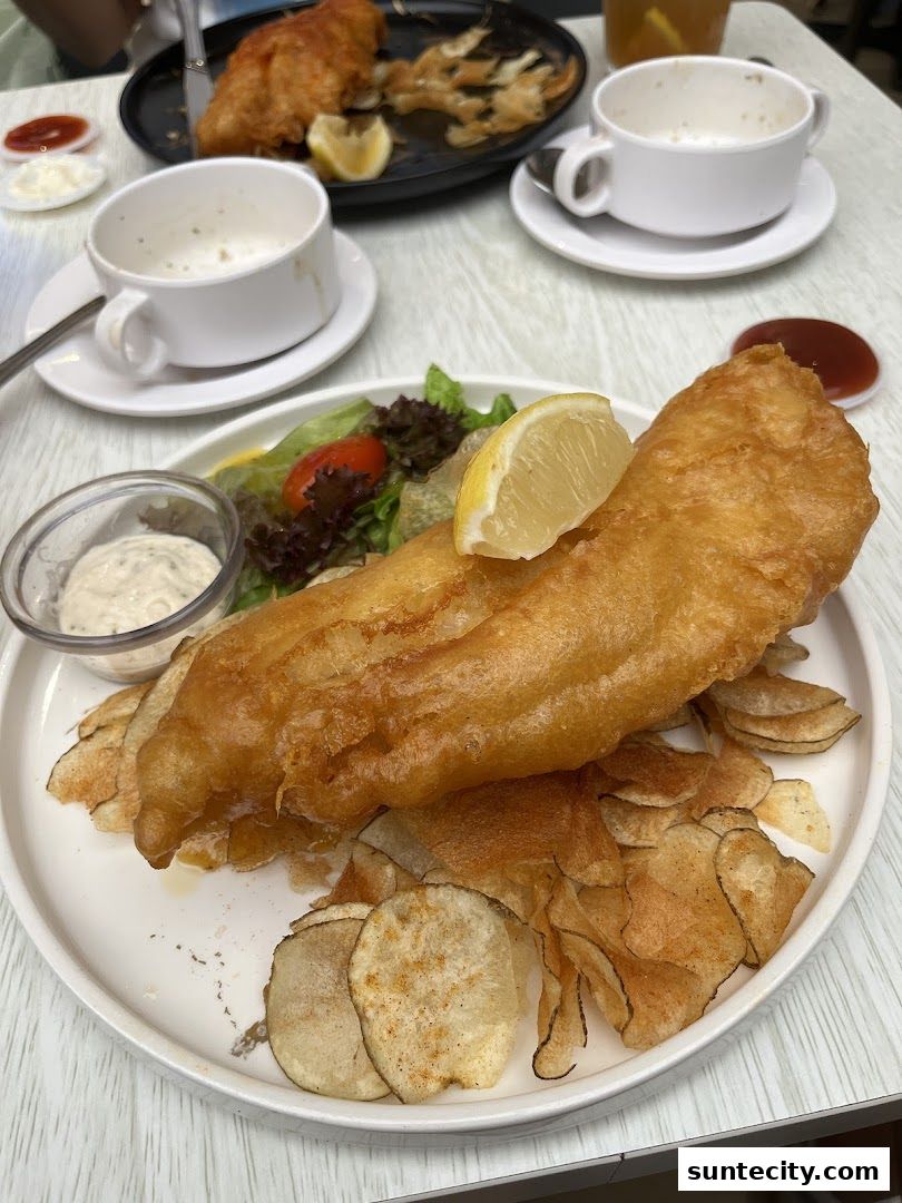 A plate of golden-brown battered fish and chips with a side salad and dipping sauce.