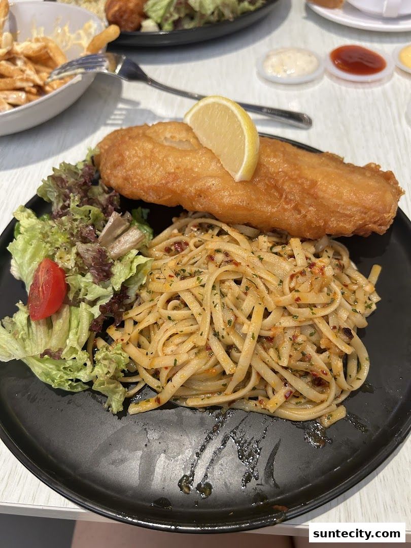 A plate of fish and chips with pasta and salad, garnished with a lemon slice.