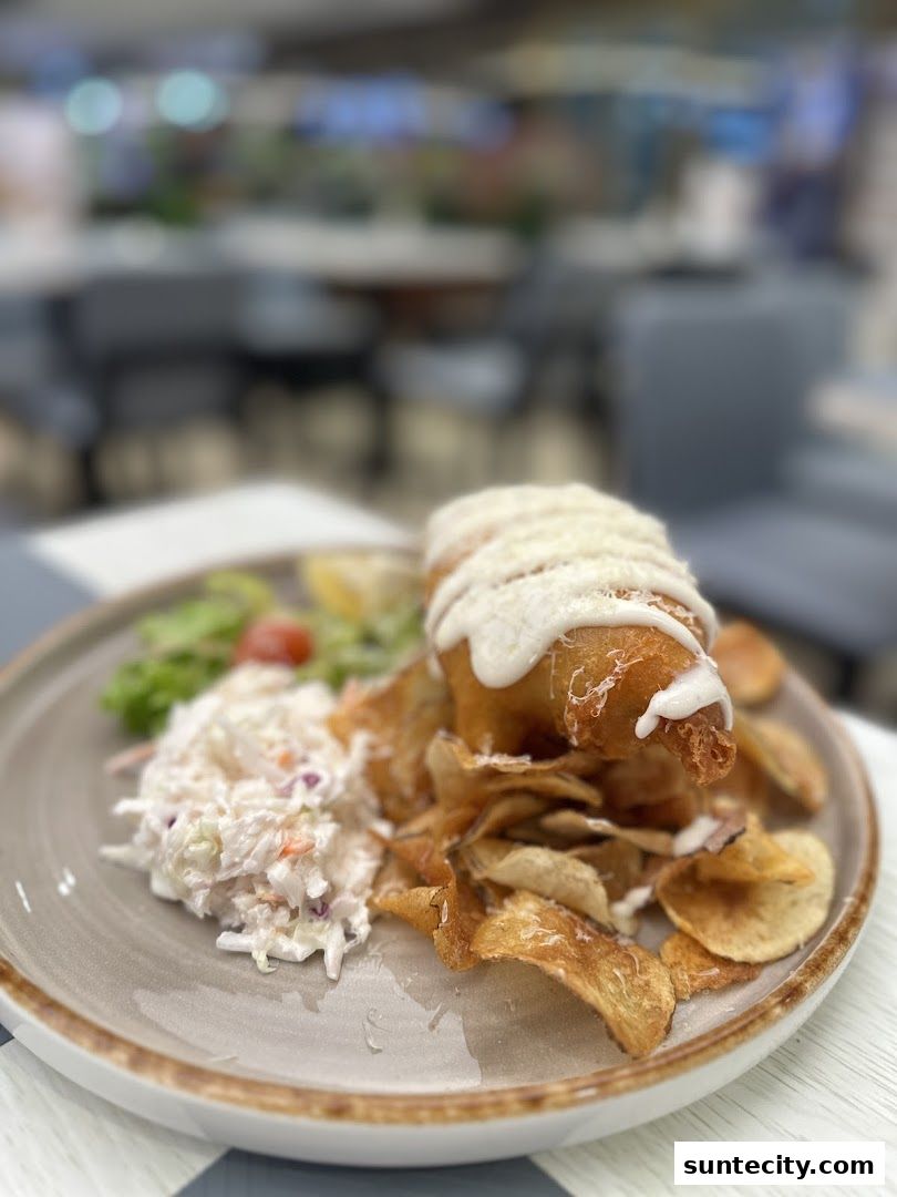 A plate of battered fish and chips with coleslaw and a lemon wedge.
