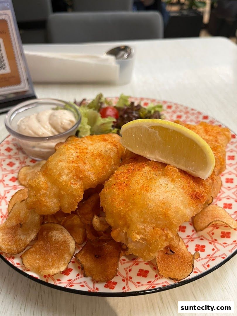 A plate of crispy fish and chips with a side of dipping sauce and salad.