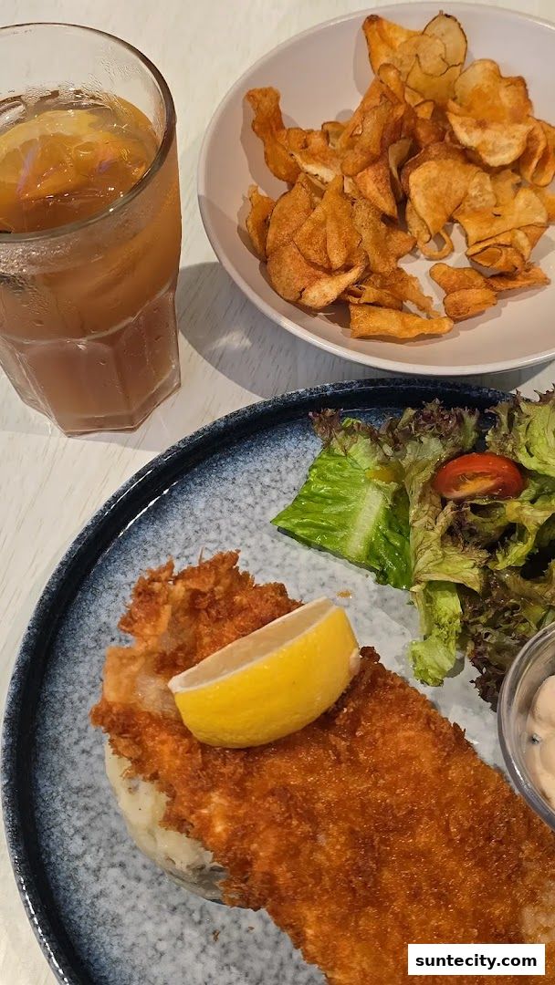 A plate of crispy fish and chips with a side salad and a glass of iced tea.