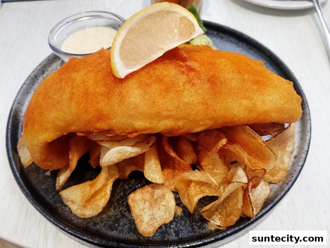 A close-up shot of a golden-brown fish and chips dish with a lemon slice and dipping sauce.