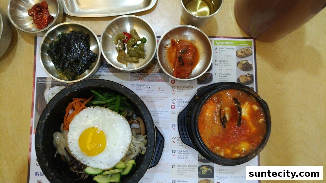 A table spread with Korean dishes including bibimbap, kimchi, and a spicy stew.