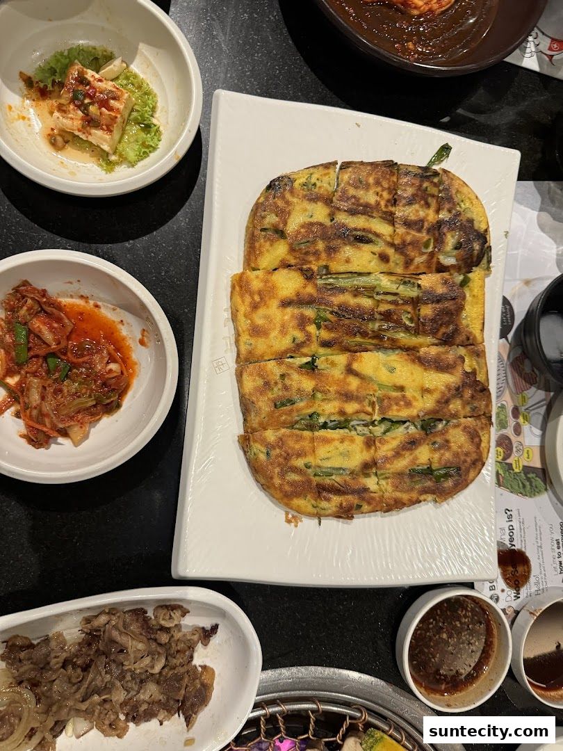 A table laden with Korean dishes, including kimchi, savory pancakes, and grilled meat.