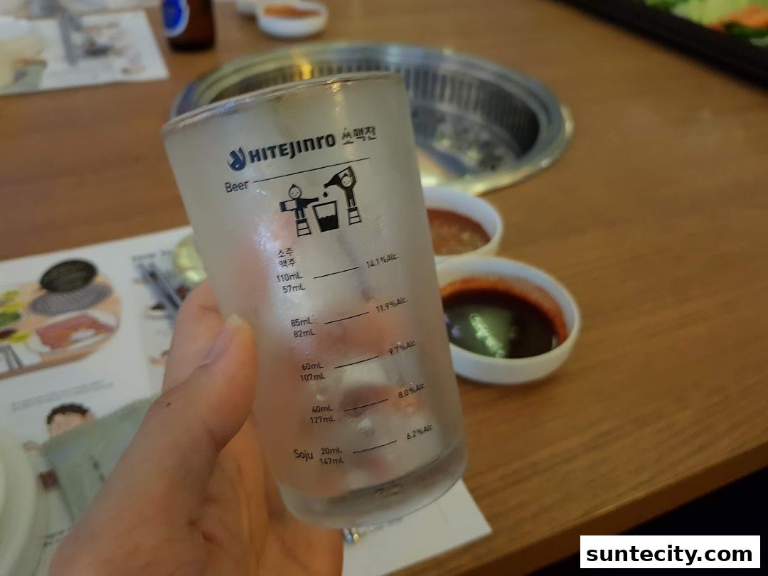 A hand holds a frosted glass with Korean text and measurement markings.