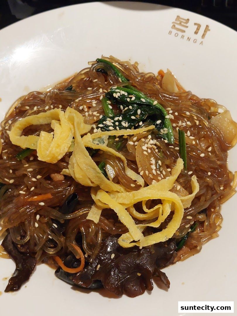 A close-up of a delicious Korean Japchae dish with noodles, vegetables, and egg garnish.