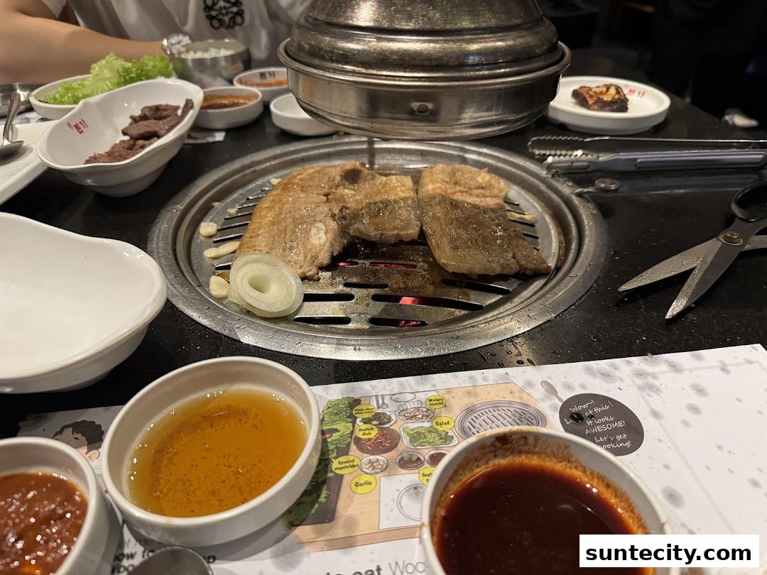A table at Bornga Singapore Suntec City with Korean BBQ being grilled, side dishes, and sauces.