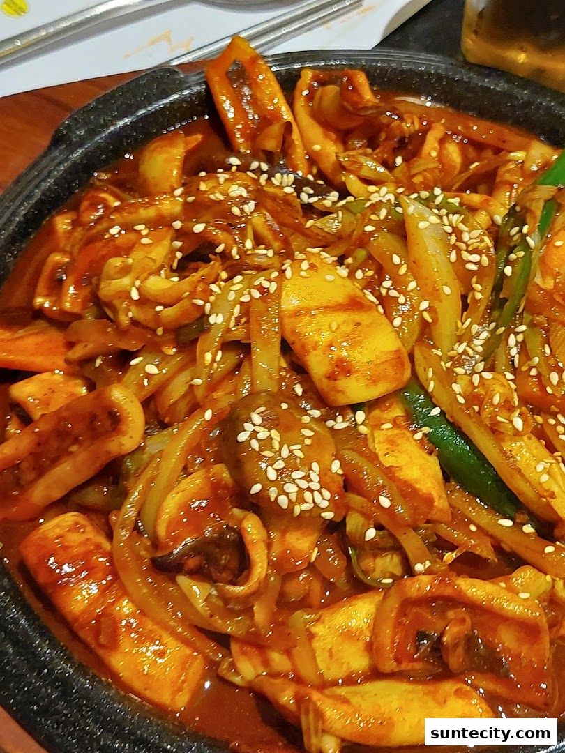 A close-up of a spicy Korean squid dish with onions and sesame seeds.