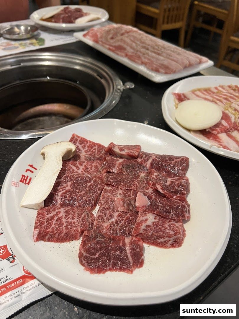 A plate of raw, marbled beef cuts and a mushroom slice, ready for grilling.