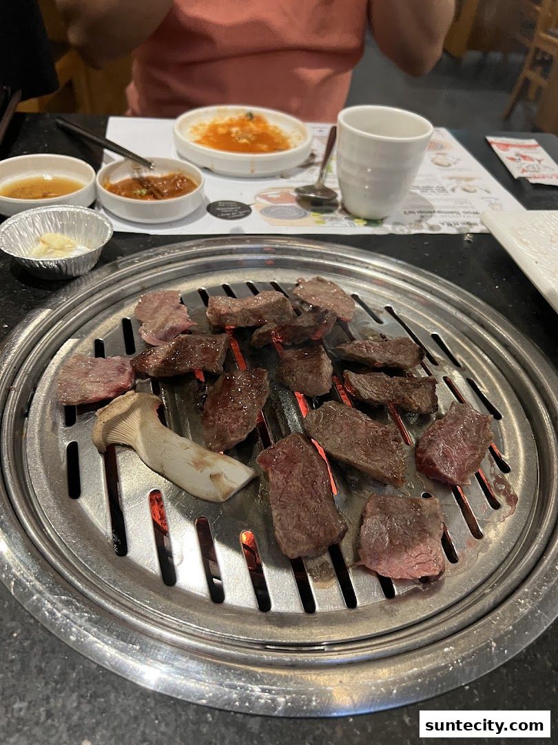 Sizzling Korean BBQ beef and mushrooms grilling over hot coals with side dishes.