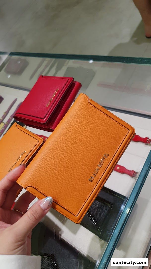 A hand holds an orange leather wallet with the Braun Buffel logo.