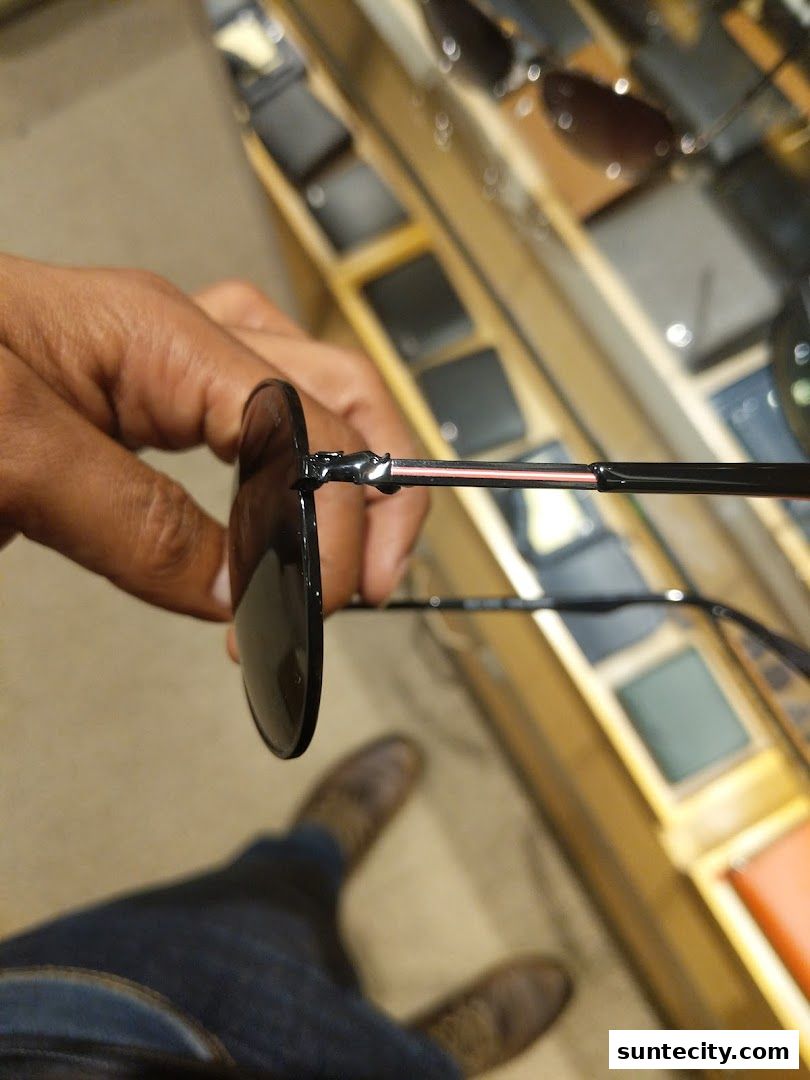 A person holds a pair of sunglasses in front of a display of wallets and accessories.