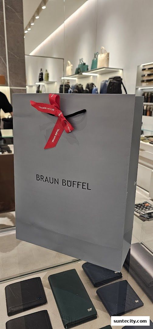 A grey Braun Buffel shopping bag with a red ribbon and wallets displayed in the foreground.