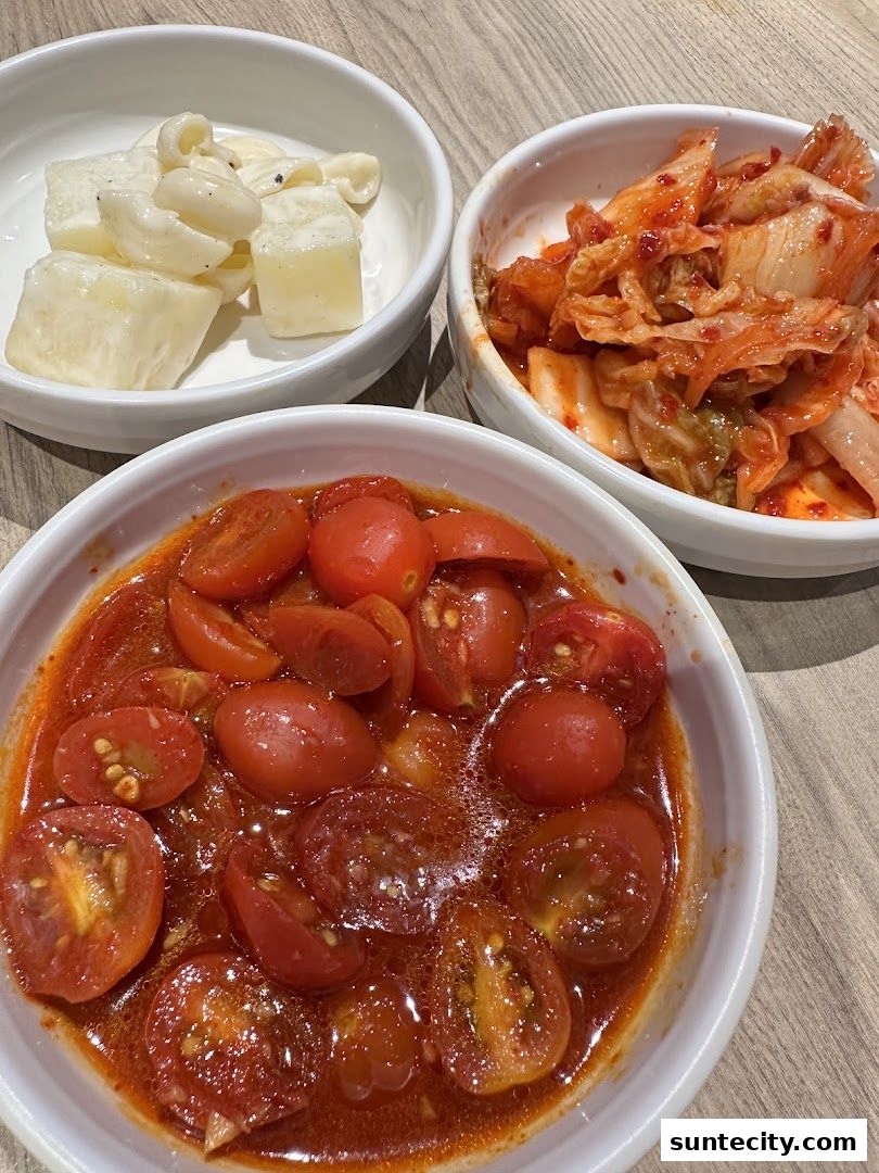 Three bowls of Korean side dishes: kimchi, cherry tomatoes in sauce, and a creamy potato salad.