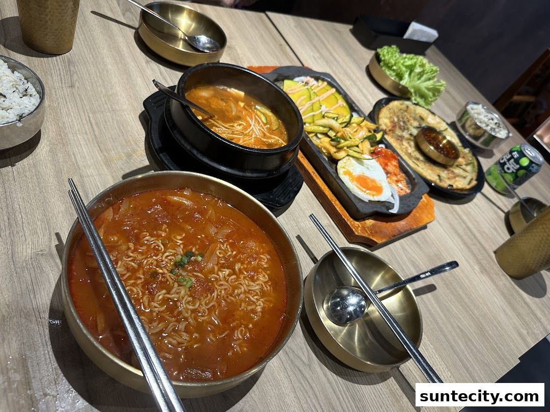 A table laden with delicious Korean dishes, including kimchi stew, ramen, and a sizzling platter.