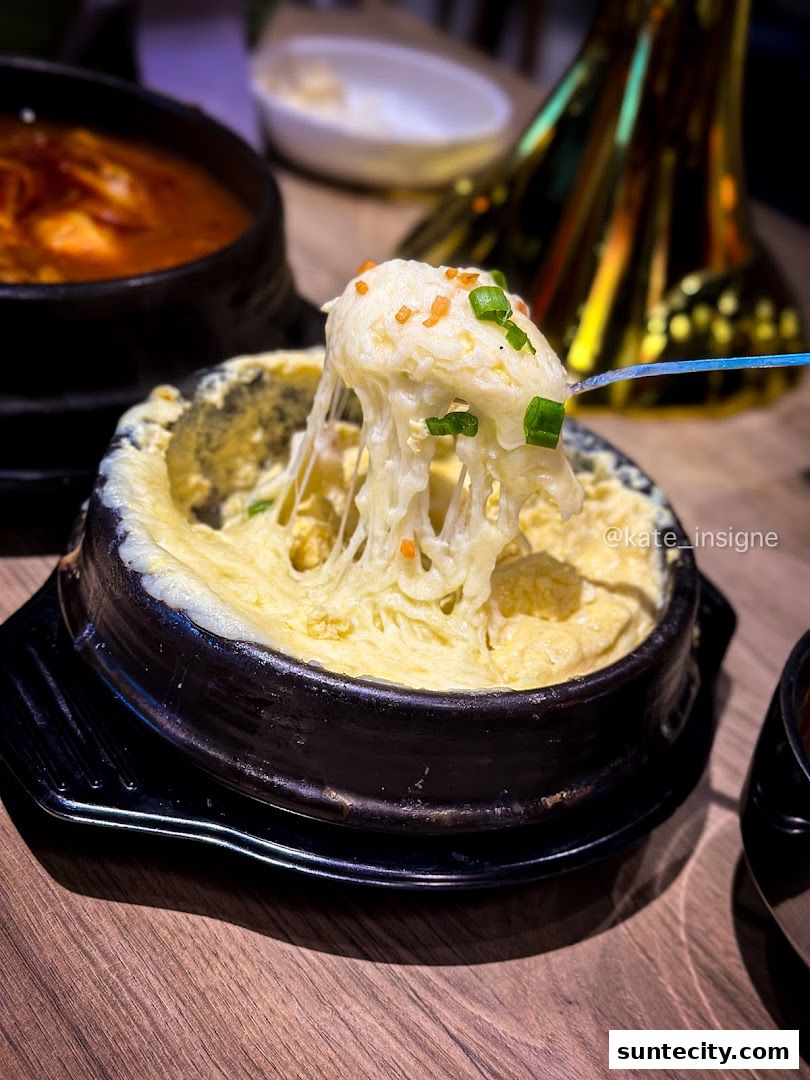 A close-up of a steaming Korean steamed egg dish with cheese and chives.