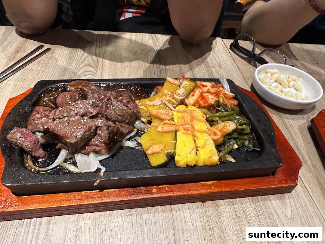 A sizzling hot plate of Korean BBQ beef with kimchi, pumpkin, and vegetables.