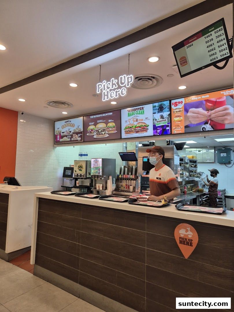 Burger King counter with staff, digital menu boards, and a 'Pick Up Here' sign.