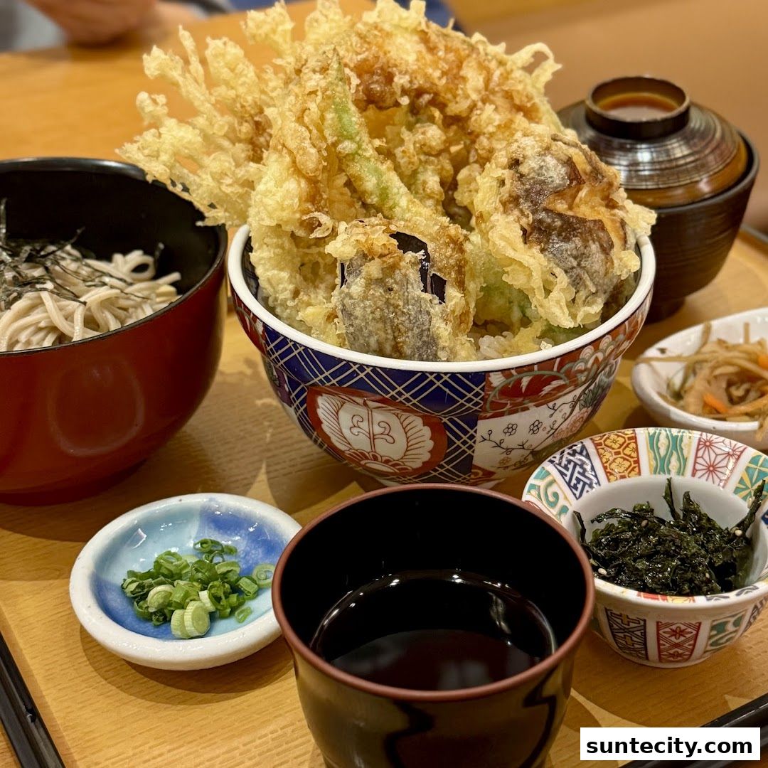 A close-up of a Japanese meal featuring tempura over rice, soba noodles, and various side dishes.
