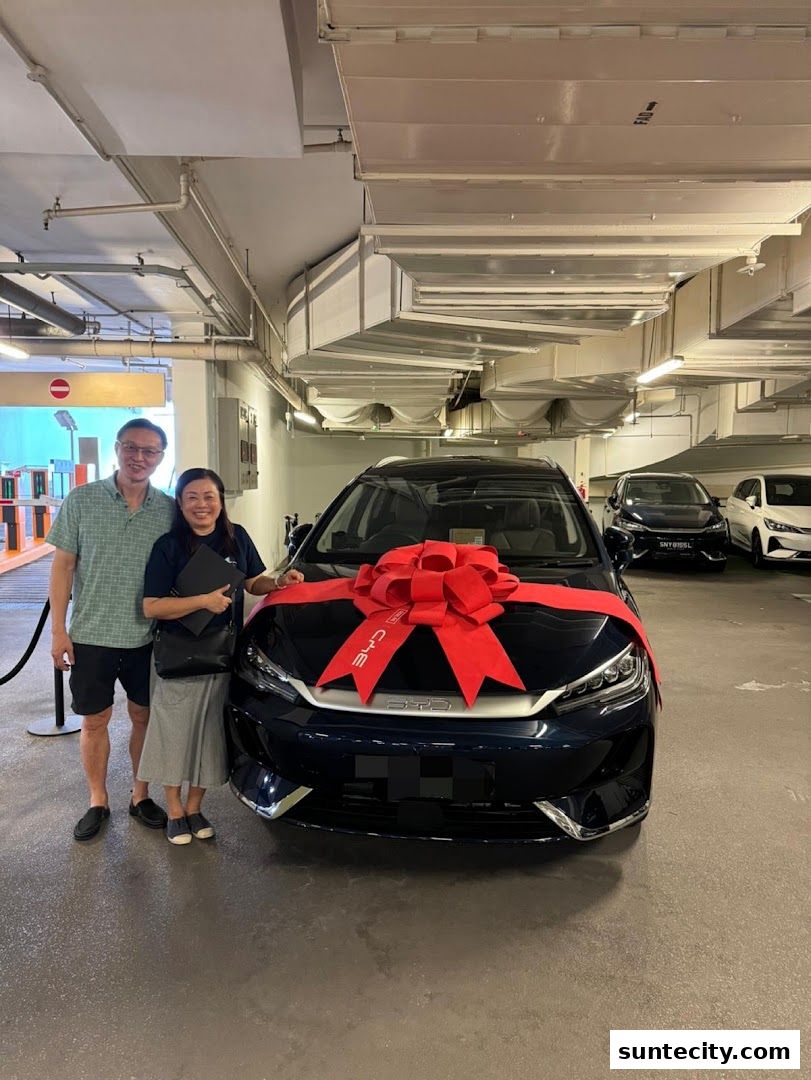 A couple poses with a new BYD car adorned with a large red bow.