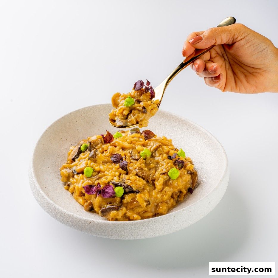 A hand holds a spoon filled with mushroom risotto, garnished with peas and herbs.