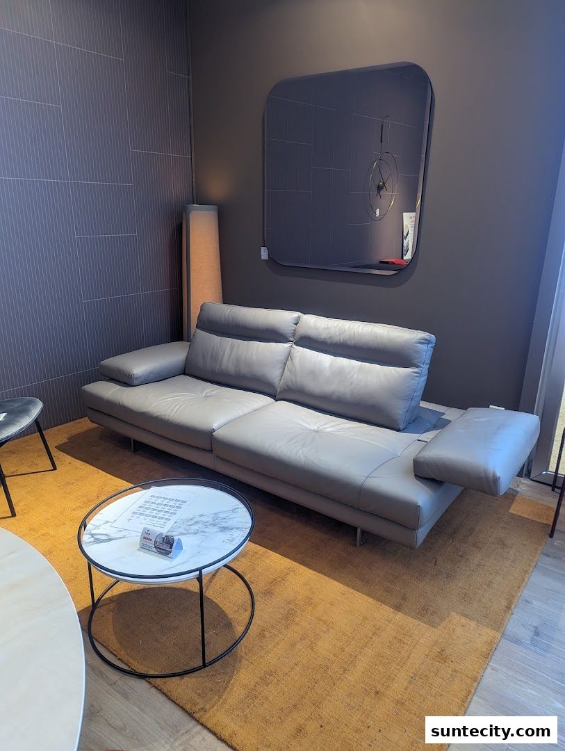 A modern grey leather sofa is displayed with a marble-top coffee table and a stylish wall clock.