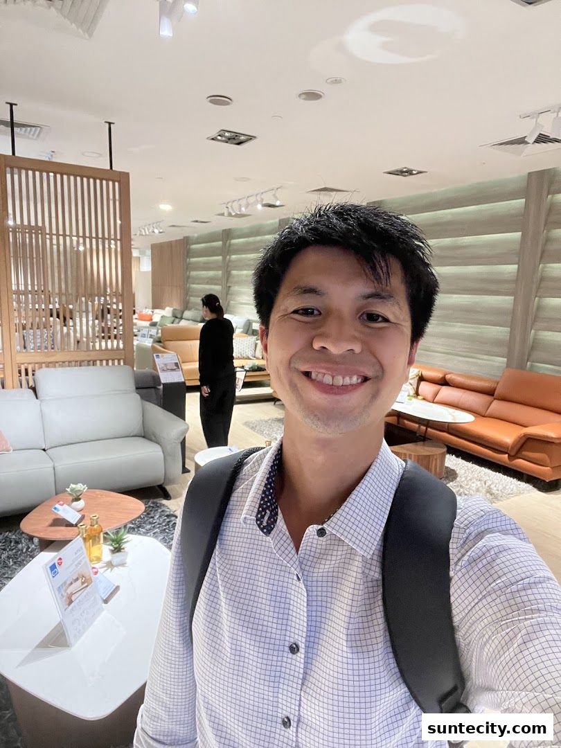 A man smiles for a selfie in a modern furniture store showcasing sofas and decor.