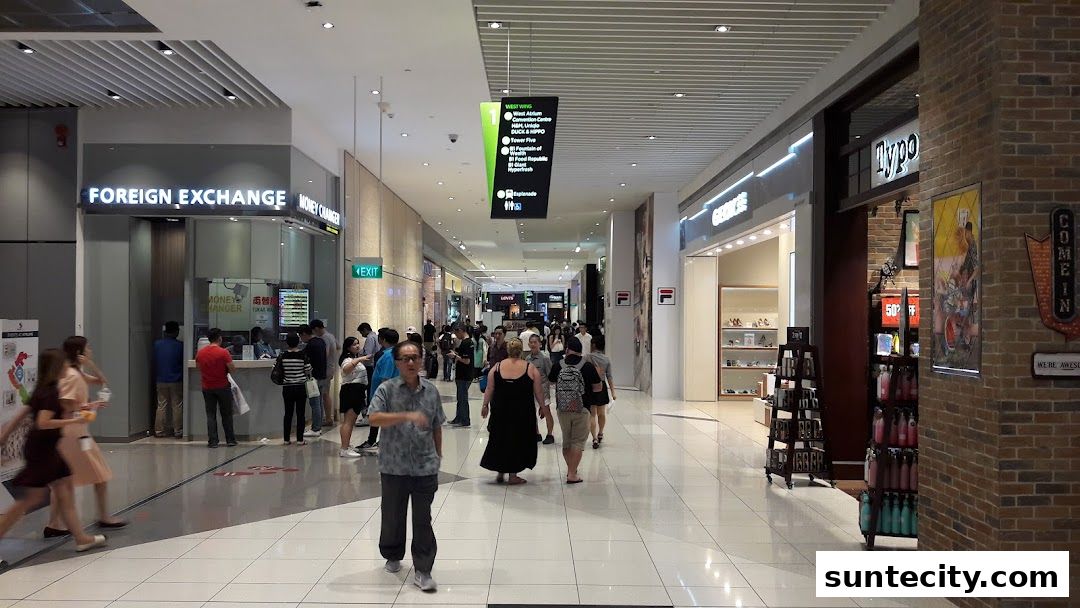 A busy shopping mall corridor with a foreign exchange counter and various shops.