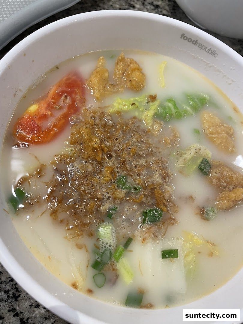 A close-up of a bowl of sliced fish soup with tomatoes, vegetables, and crispy toppings.