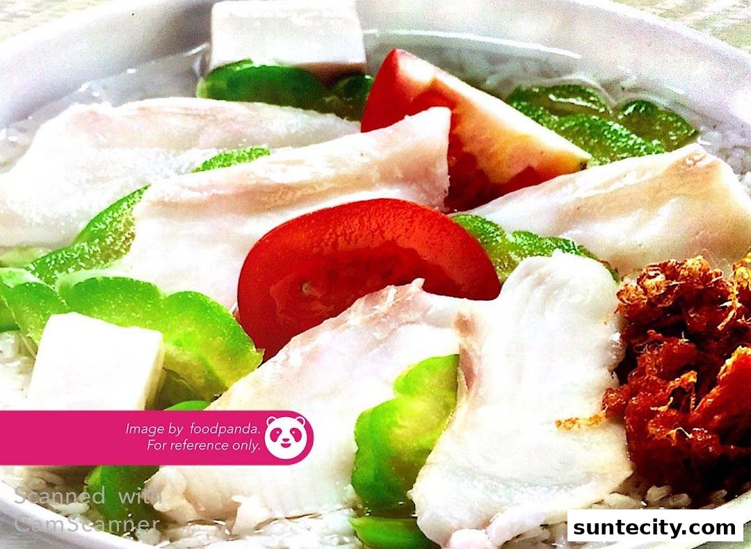 A close-up of a bowl of sliced fish soup with tomatoes, green peppers, and tofu.