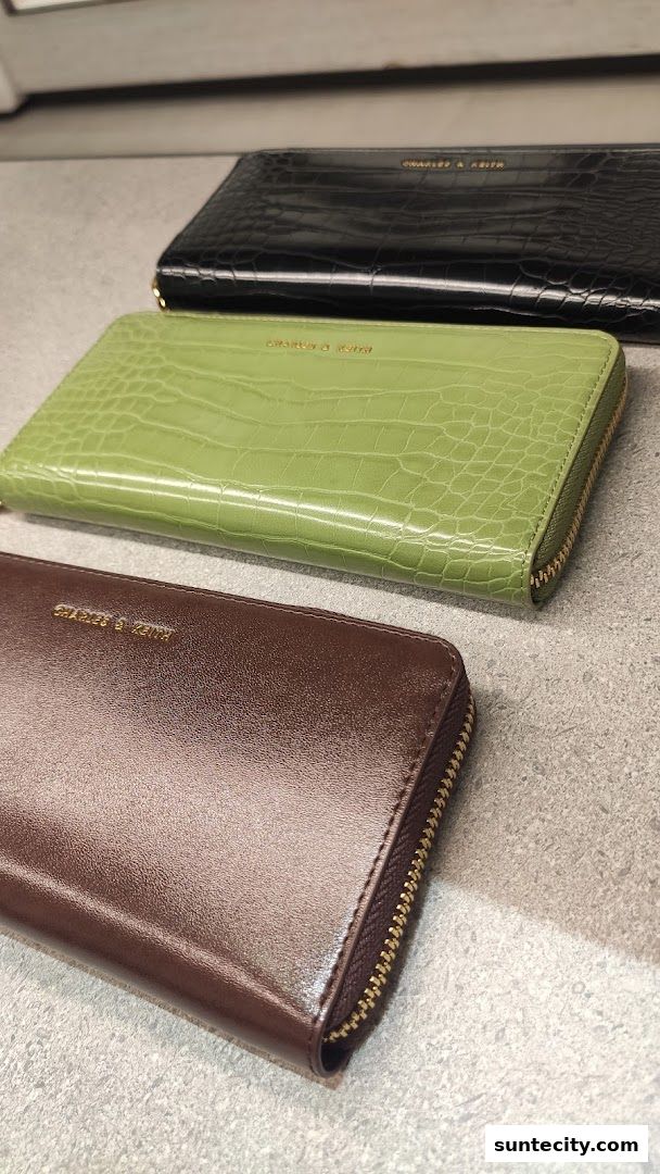 Three stylish Charles & Keith wallets in black, green, and brown with crocodile texture.