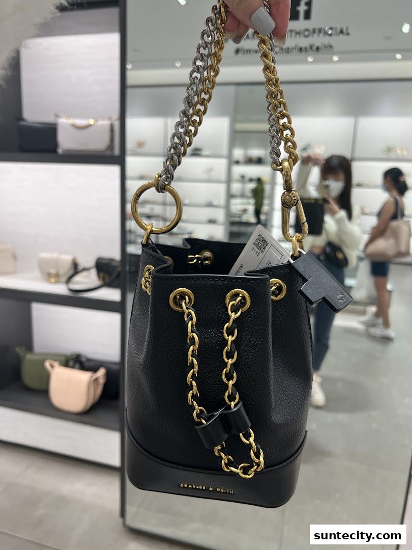 A person holds a black bucket bag with gold and silver chain straps inside a Charles & Keith store.